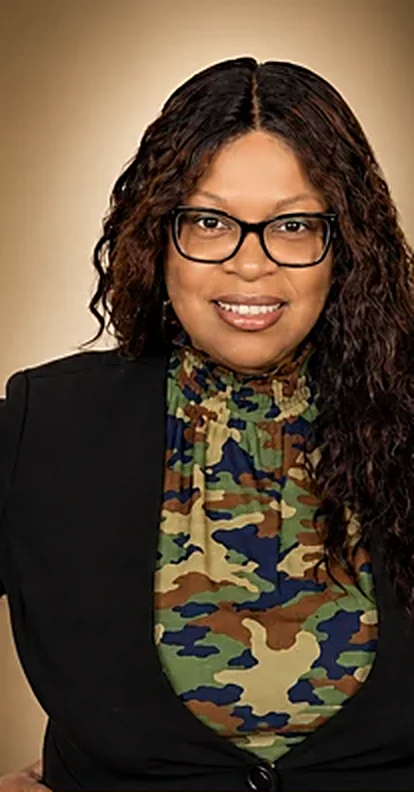 Portrait of MaShay Curtis smiling, wearing glasses and a black blazer